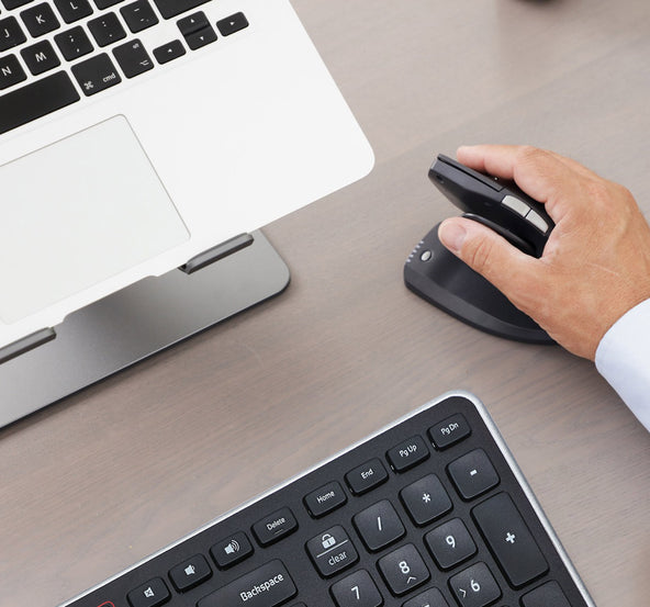 a detailed photo of a laptop on a laptop stand, a hand on a vertical ergonomic mouse and a keyboard on a desktop